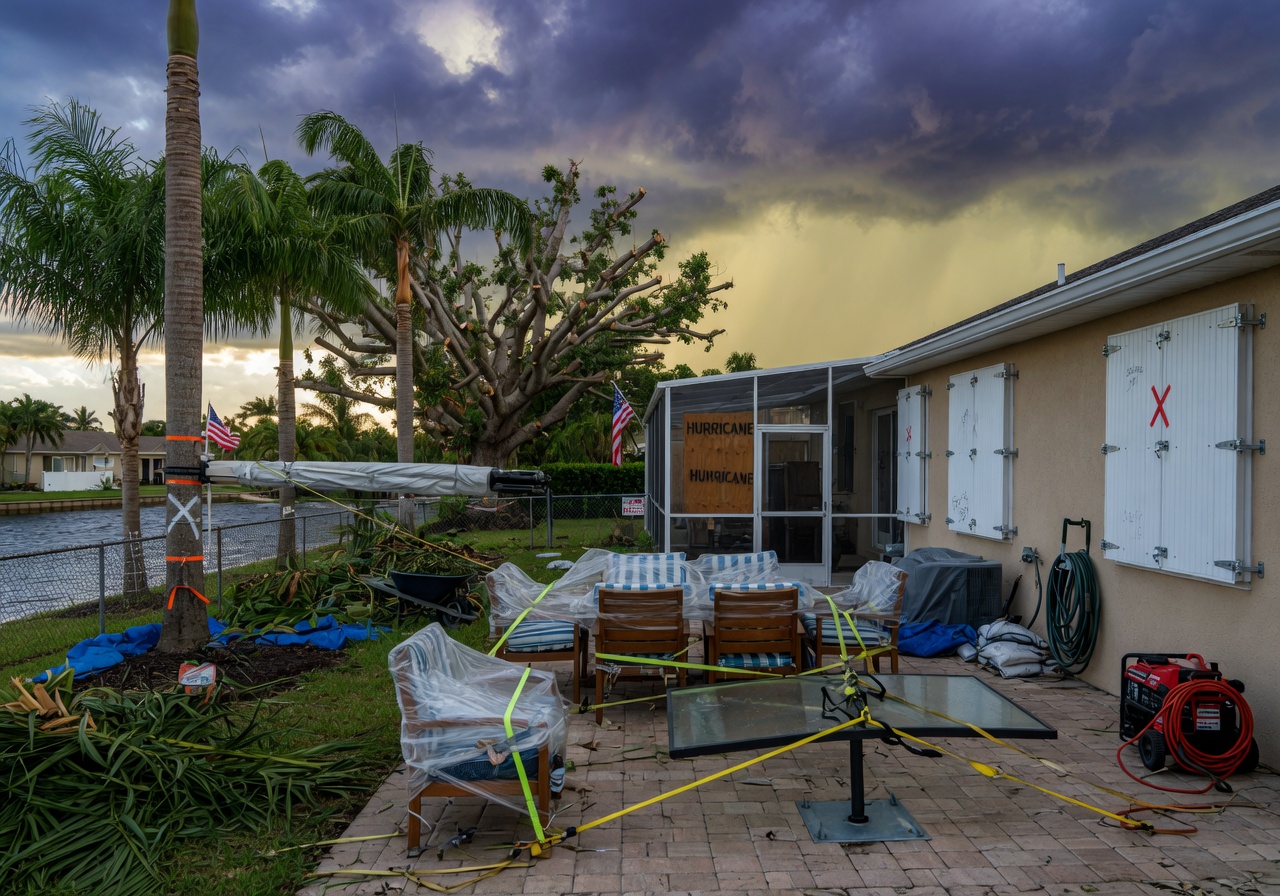 Storm preparation in Cape Coral backyard showing secured outdoor furniture, pruned trees, and secured hurricane shutters on home, dramatic sky, ultra-realistic 8K photograph